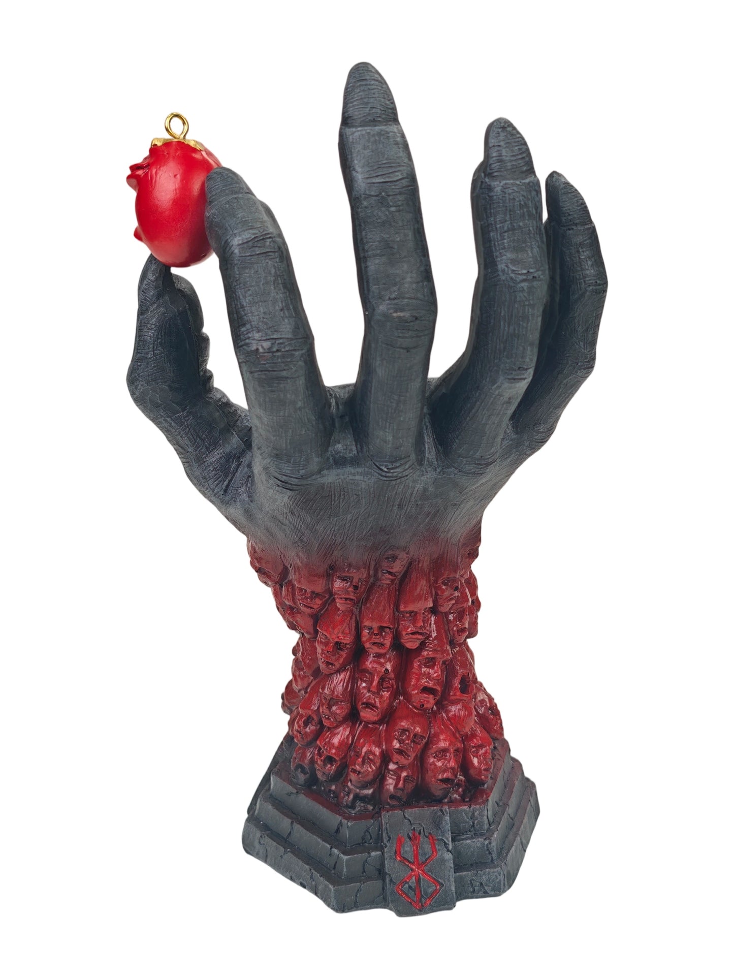 A gothic-style hand sculpture holding a small red rose ornament, with the hand transitioning into a base of many faces, on a plain white background.