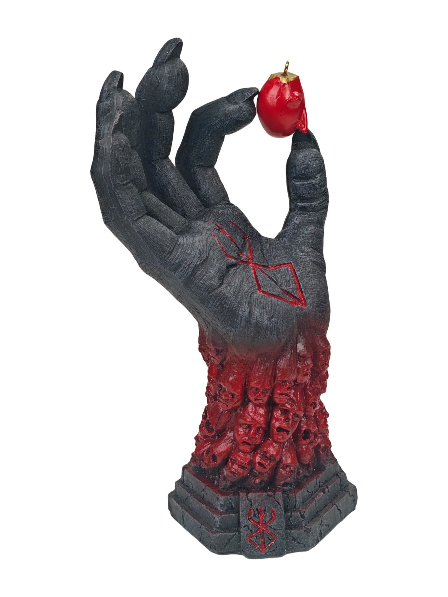 A gothic horror figurine of a skeletal hand holding a red hot pepper, with a base of skulls and red markings, isolated on a white background.