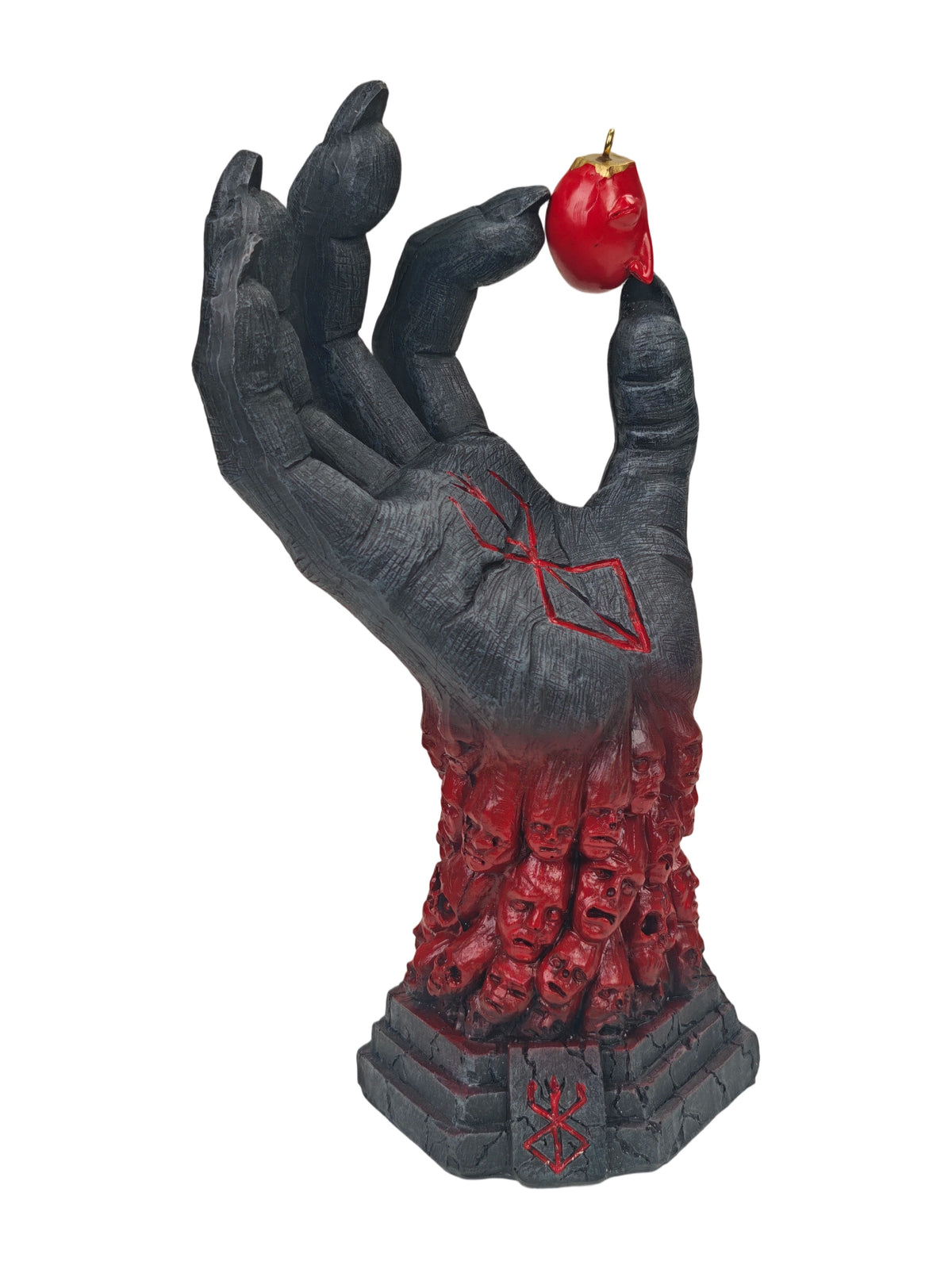 A gothic horror figurine of a skeletal hand holding a red hot pepper, with a base of skulls and red markings, isolated on a white background.