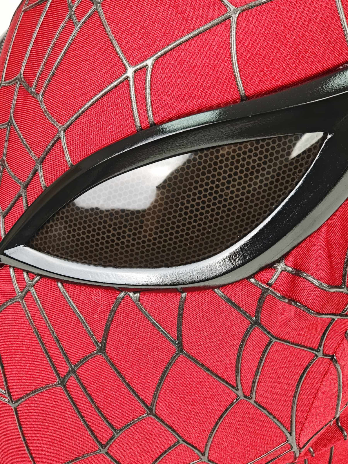 Macro view of dark honeycomb eye lens and red webbed fabric on Superior Spider-Man mask